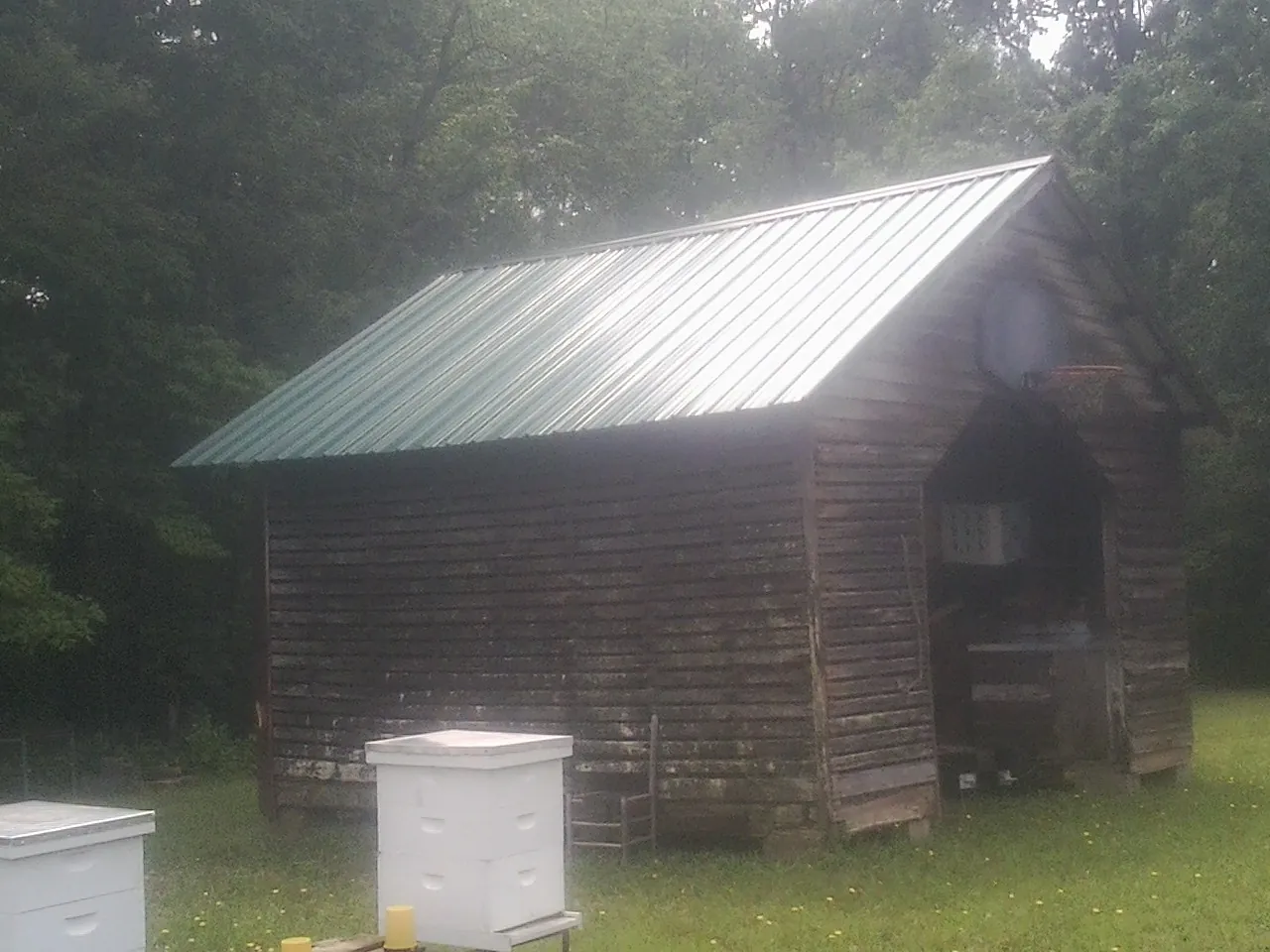 Green metal roof on a weathered barn beside stacked beehives in Andover